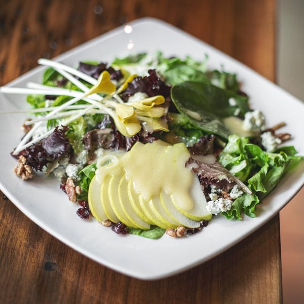 Gourmet salad featuring mixed greens, sliced pears, blue cheese, walnuts, and sprouts with dressing.