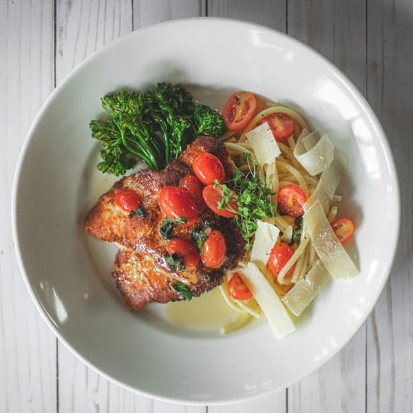 Golden chicken cutlets topped with tomatoes, broccolini, and spaghetti with shaved parmesan cheese.