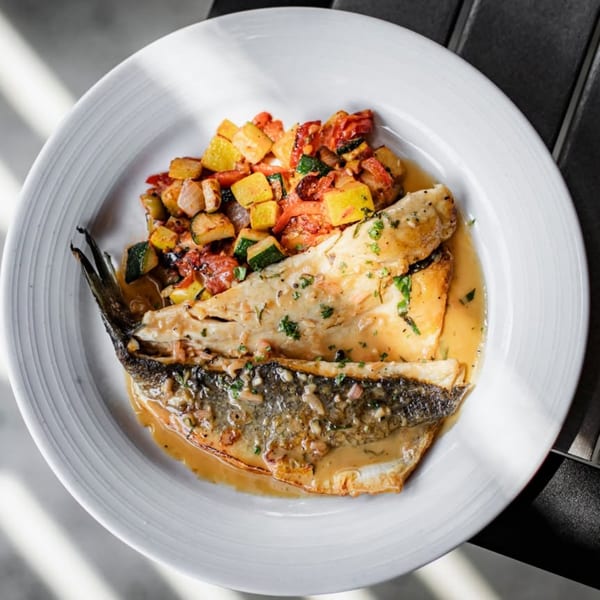 Whole roasted fish with a light sauce and a side of colorful diced vegetables on a white plate.