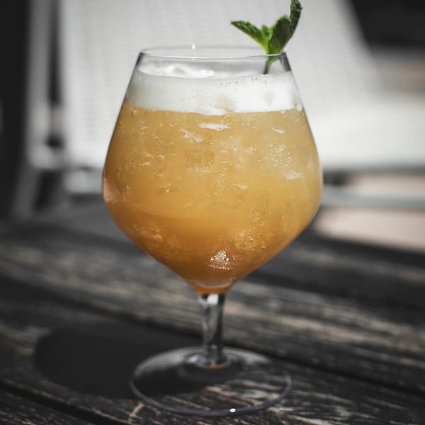Foamy orange drink with a mint garnish on a wooden table.