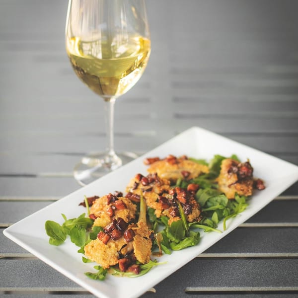 Crispy bites with a savory topping on arugula, paired with a glass of white wine.