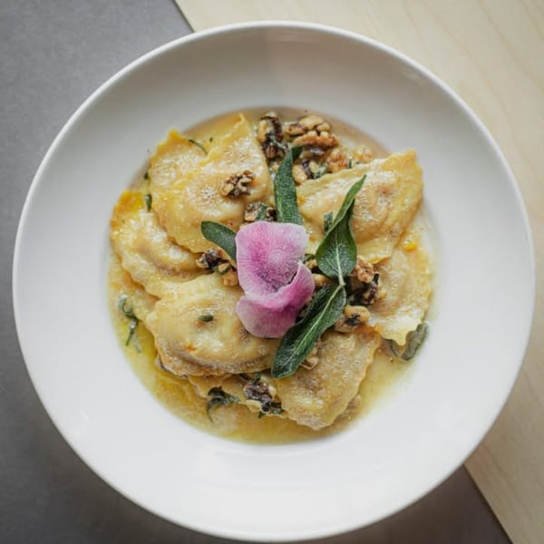 Plate of ravioli with walnuts, sage, and a pink flower in a light sauce.