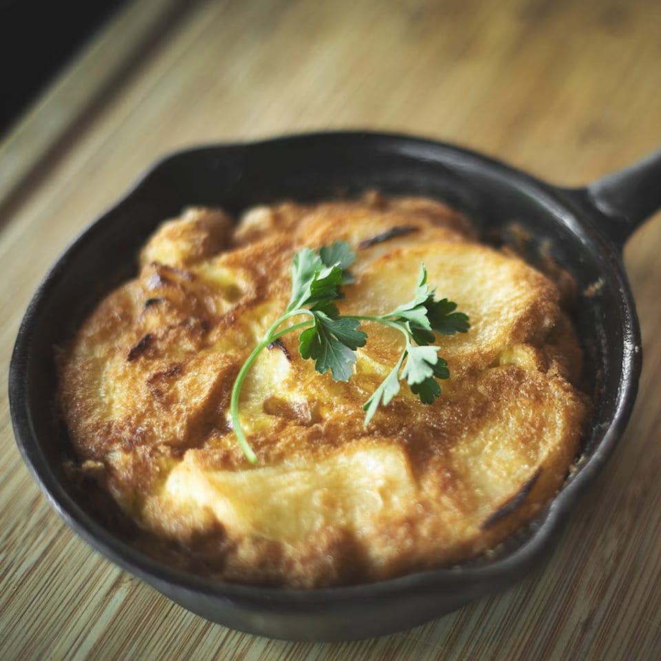 Golden brown baked egg dish in a cast iron skillet, garnished with parsley.